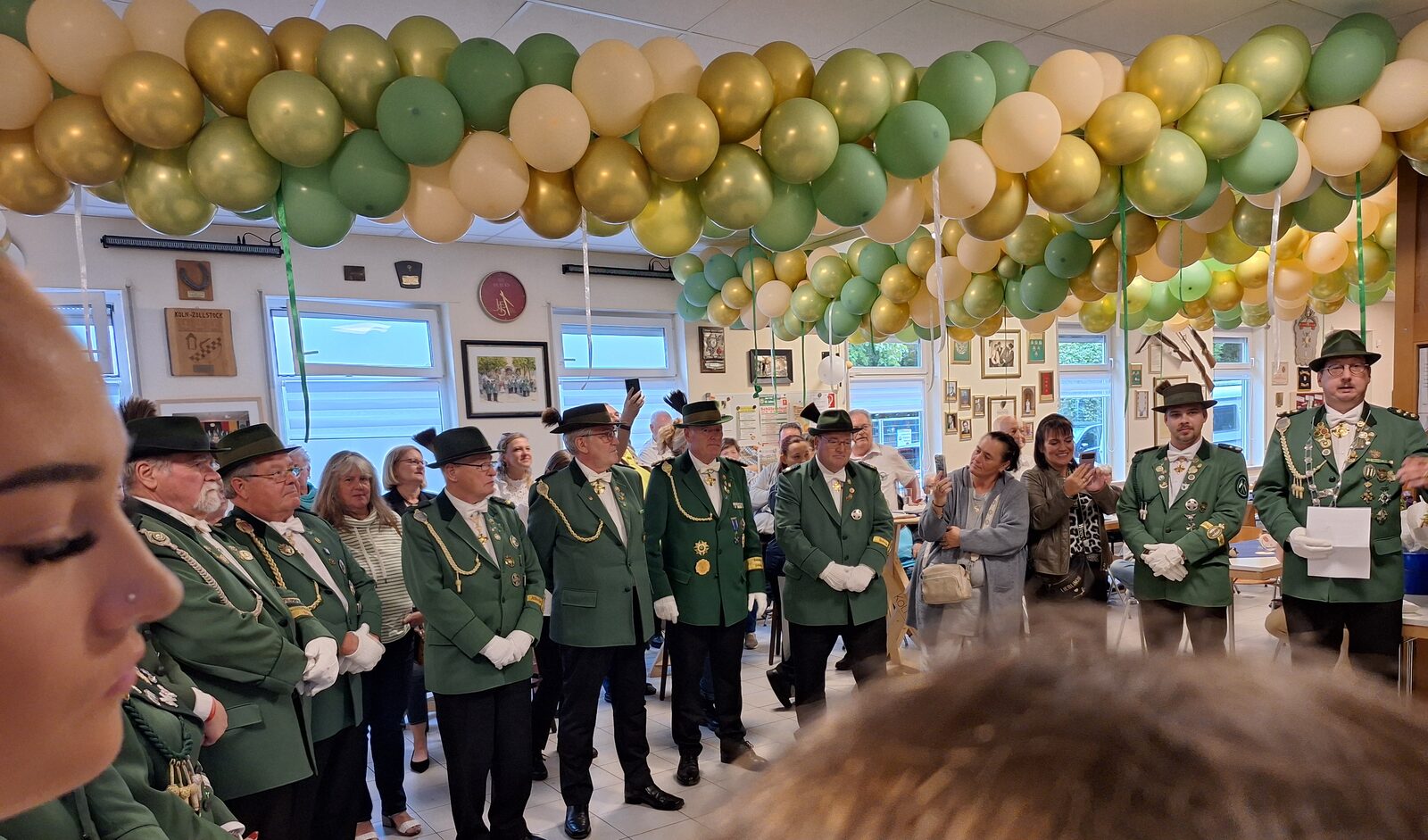 Schützen in grüner Uniform mit Federhut im Vereinsheim, darüber ein Bogen aus grünen, weißen und goldenen Luftballons